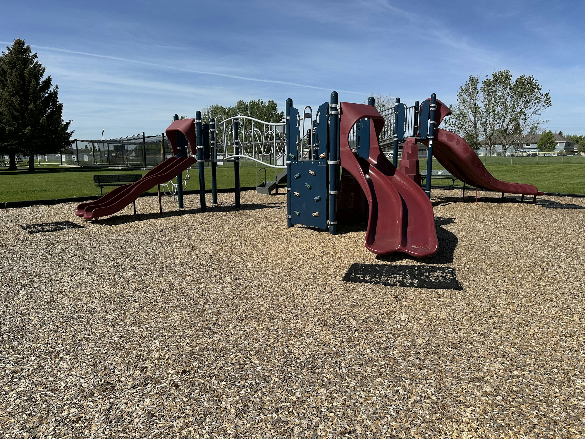 A playground with slides, climbing structures, and wood chips on a sunny day.