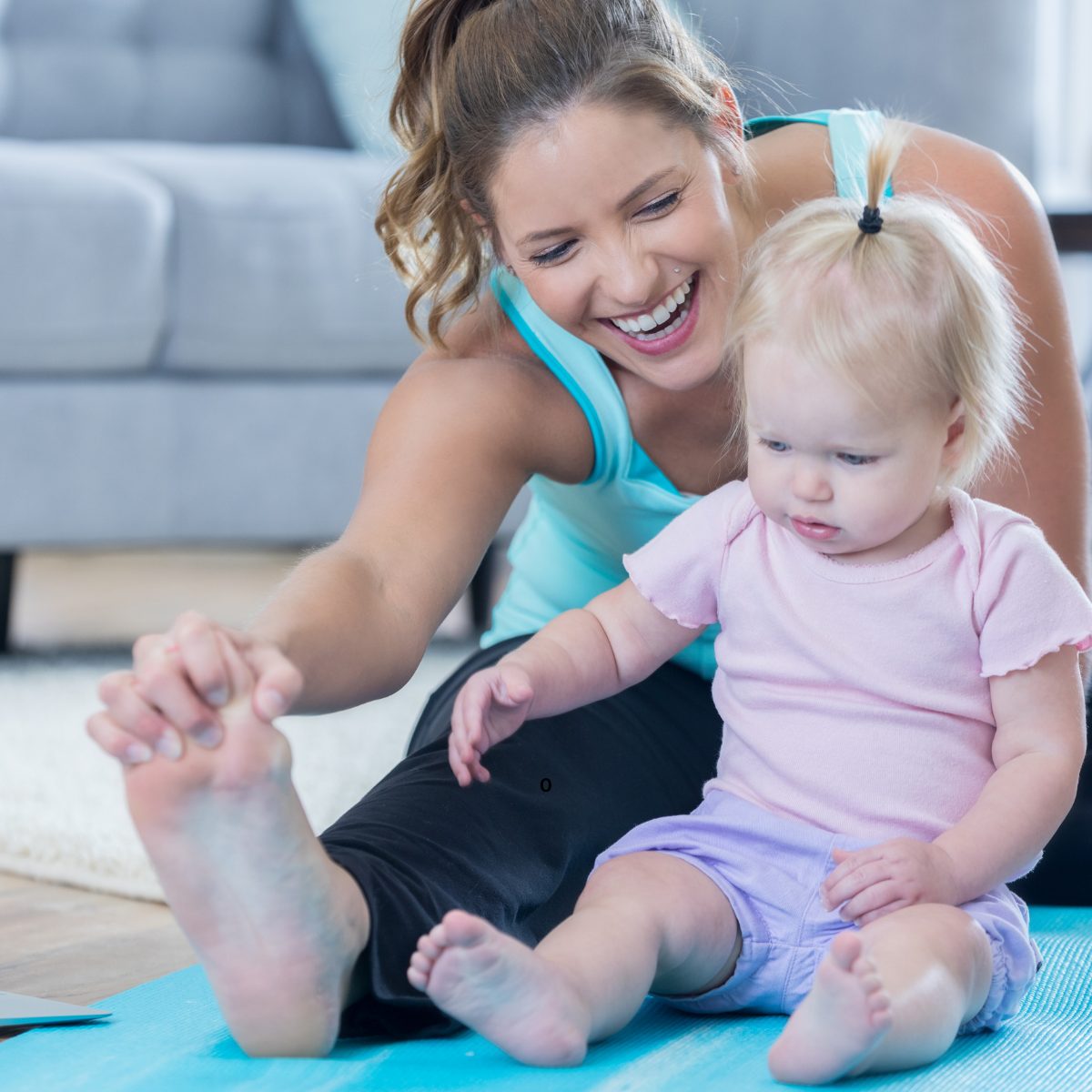 A woman and a baby sitting on a yoga mat, smiling and stretching together.