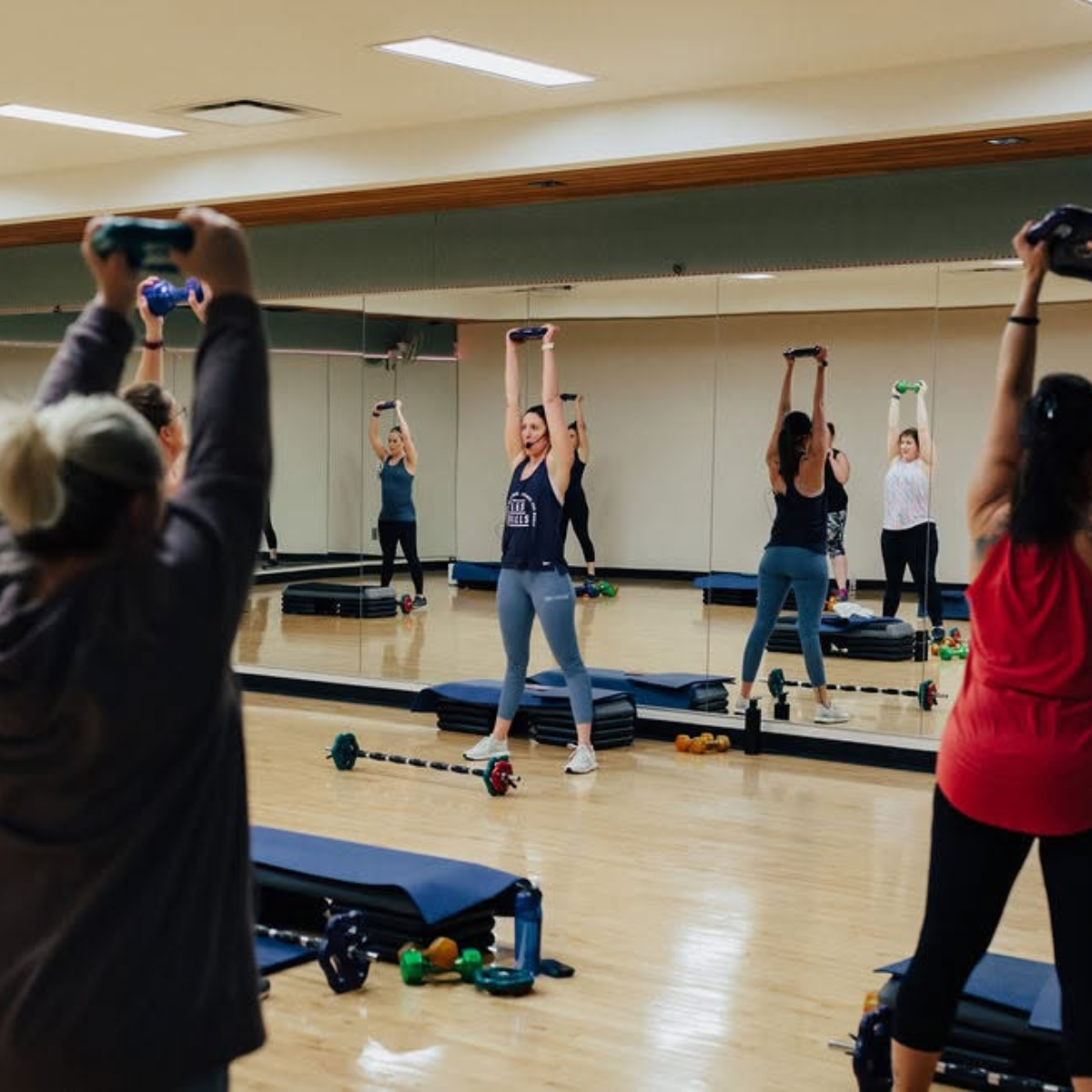 A group workout class with women lifting weights in front of mirrors in a fitness studio. Energy and focus are evident!