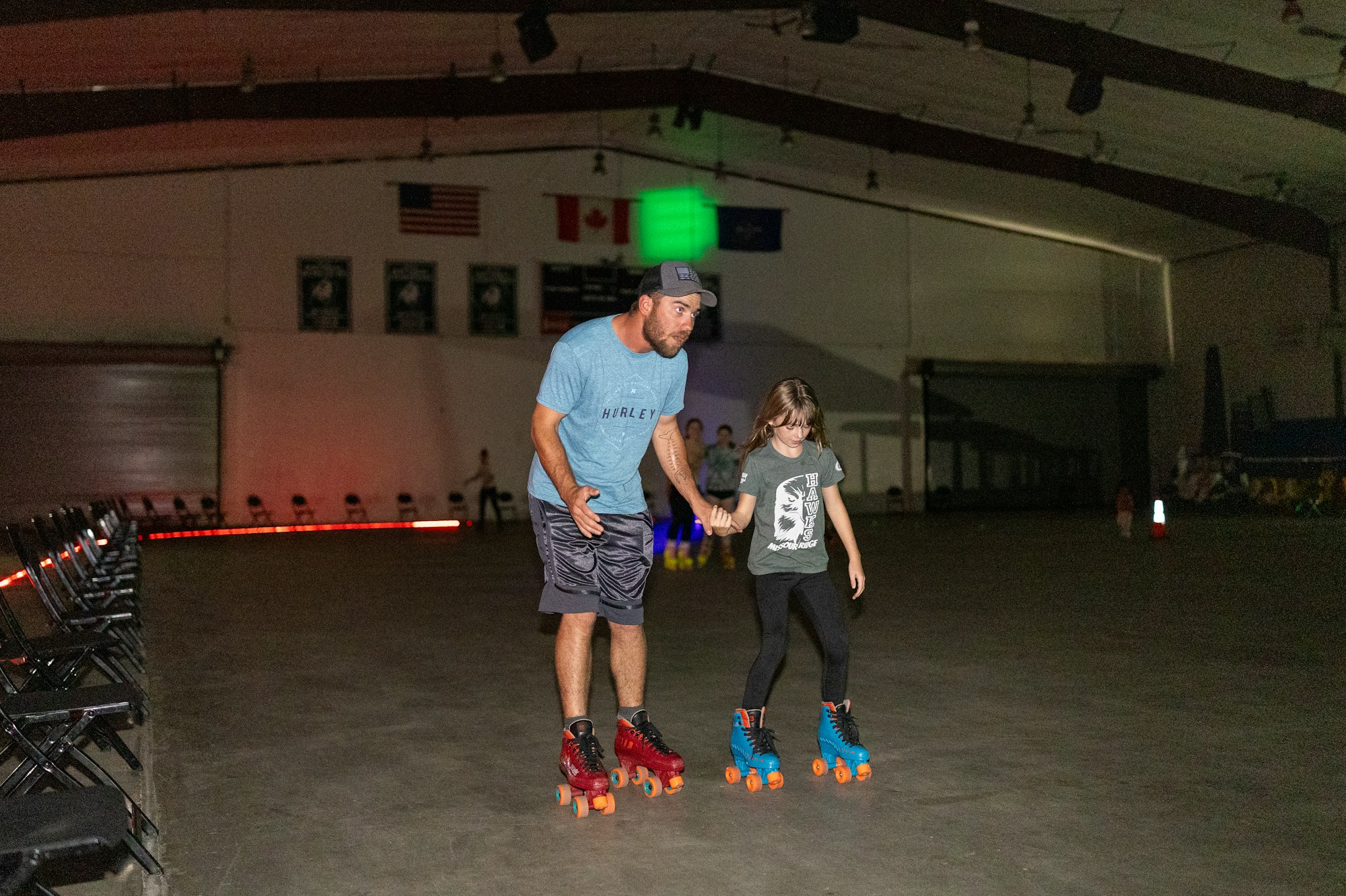 Man and child roller skating in a dimly lit indoor rink.