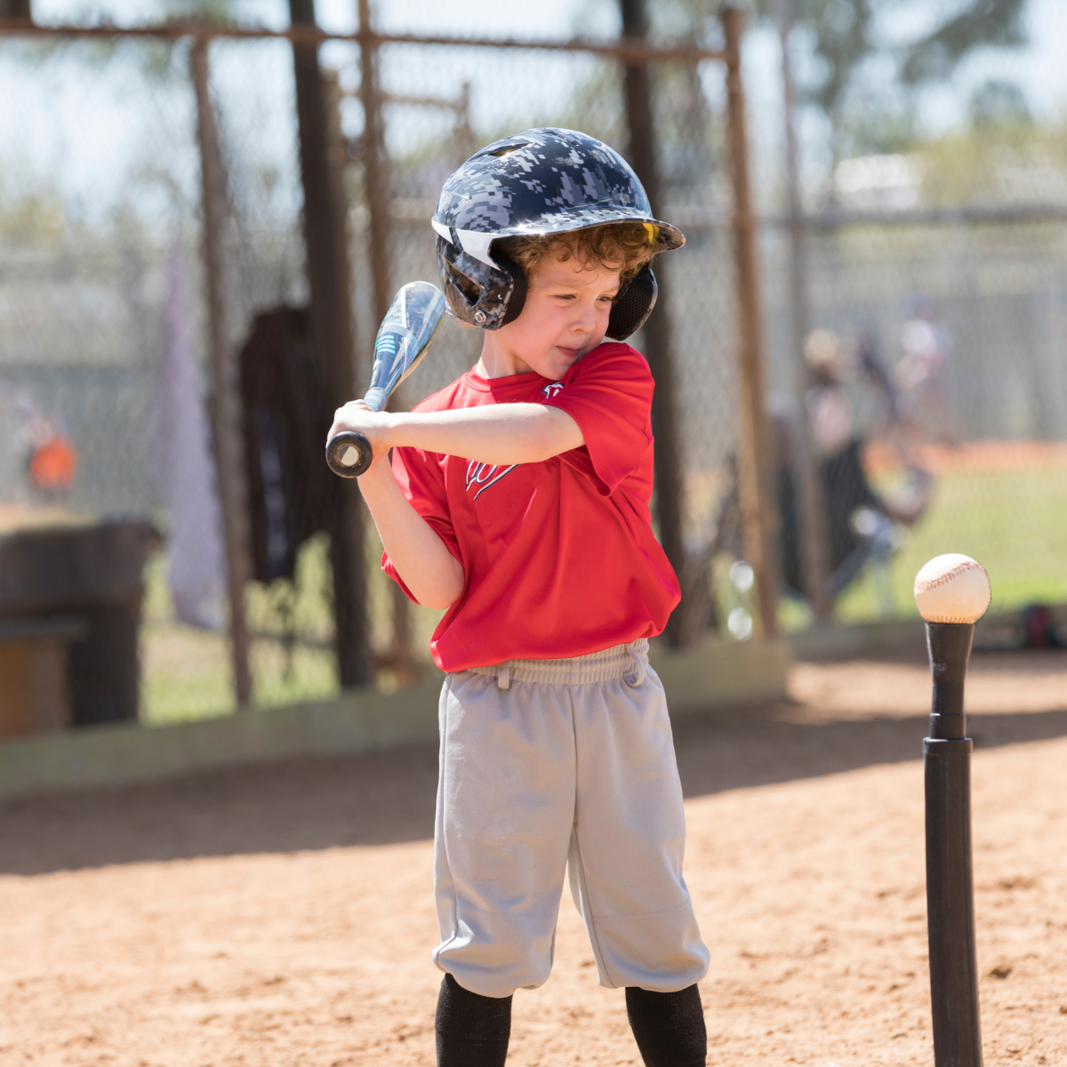 A child in a baseball uniform preparing to swing at a ball on a tee.