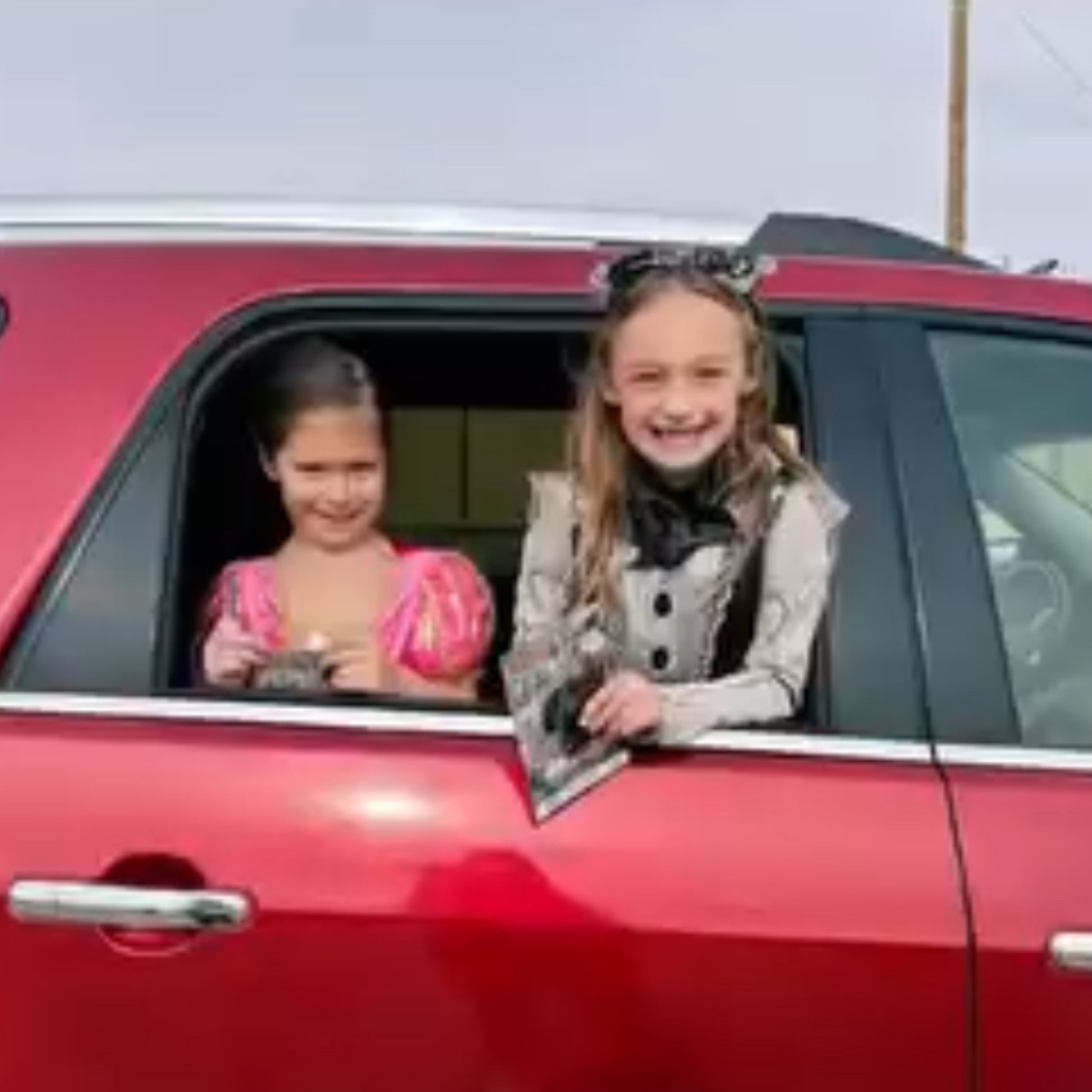 Two children are smiling while leaning out of a car window.