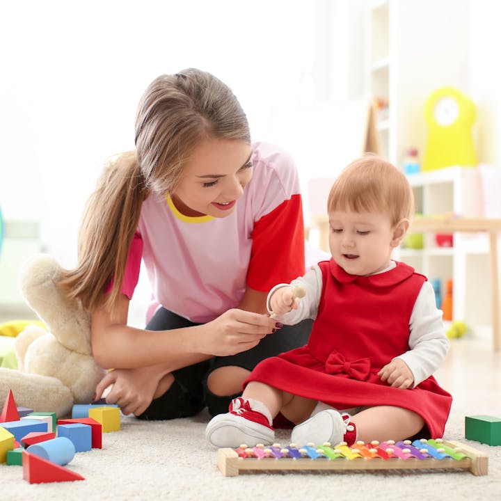 A woman and a baby play with colorful toys on a rug in a bright room.