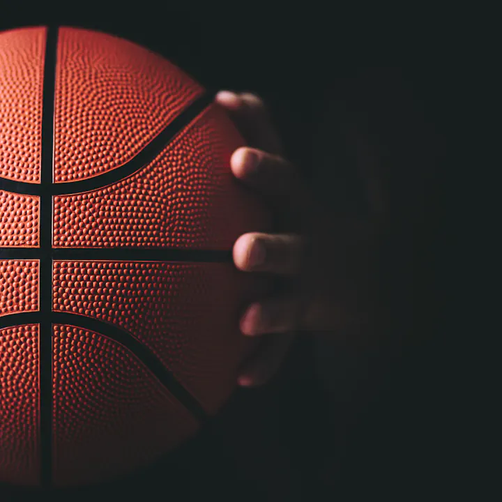 A hand gripping a basketball against a dark background.