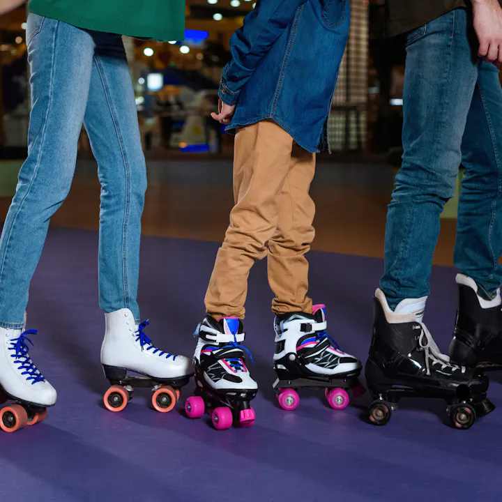 Four people are roller skating, standing side by side on a purple floor, showcasing colorful skates in a lively indoor setting.