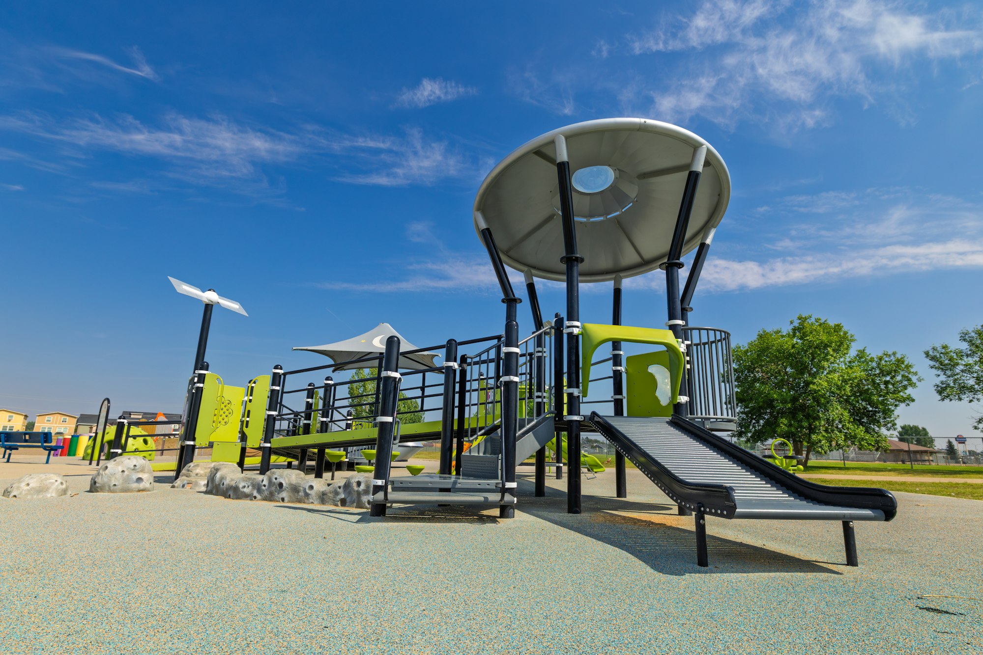 A modern playground featuring slides, climbing features, and a large canopy, set against a clear blue sky.