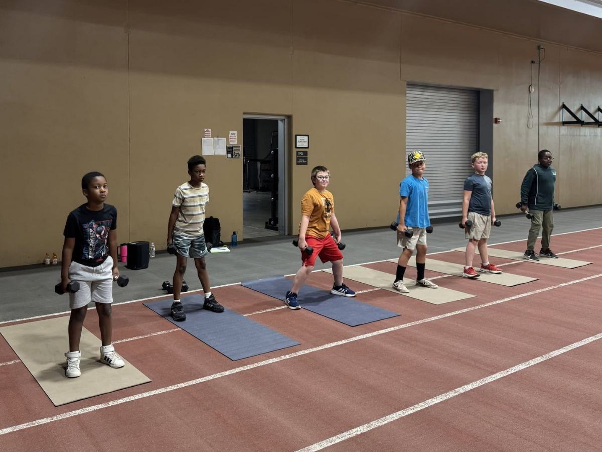 A group of kids are exercising indoors, each holding dumbbells and standing on mats, focused on their workout.