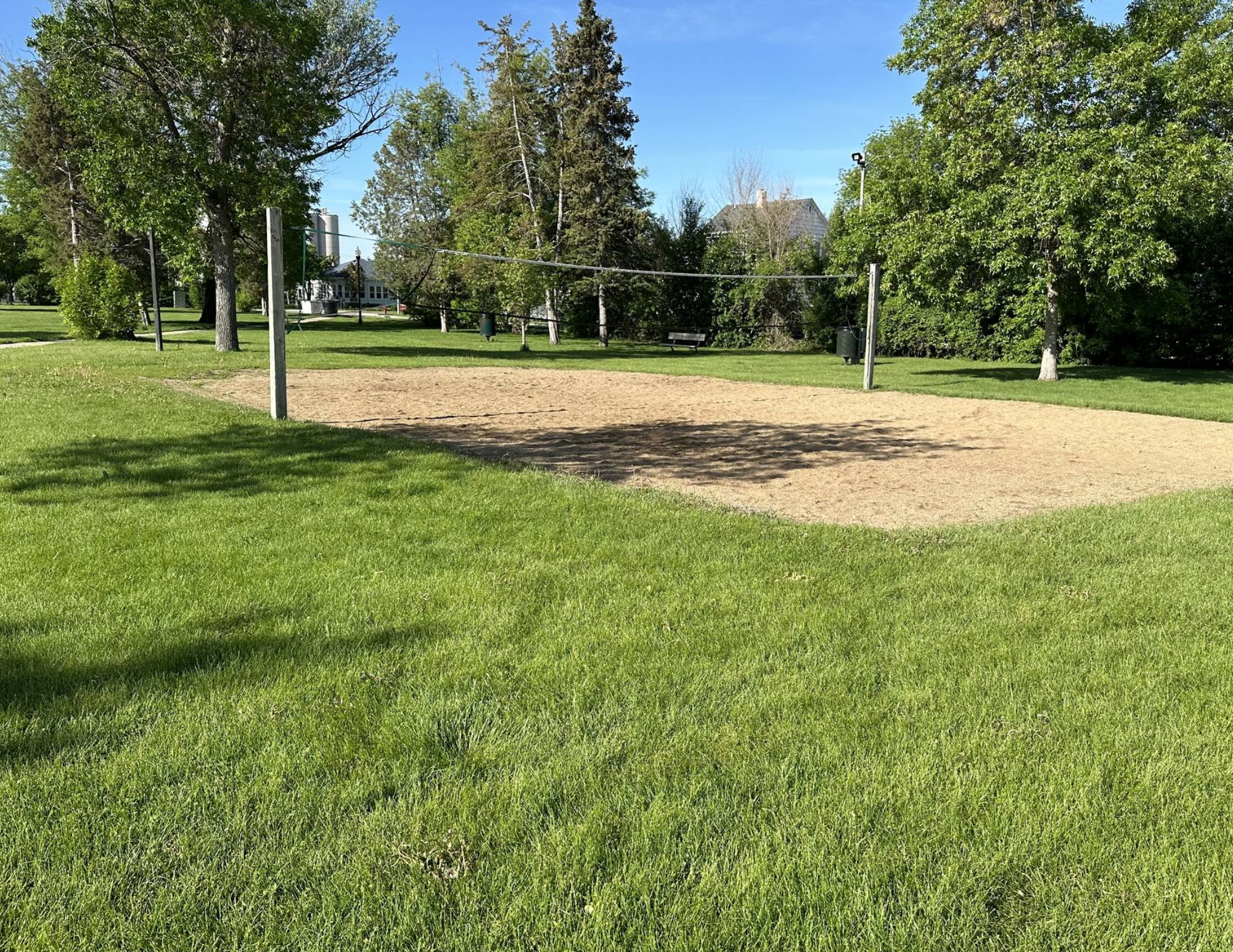 A sandy volleyball court with a net, surrounded by green grass and trees.
