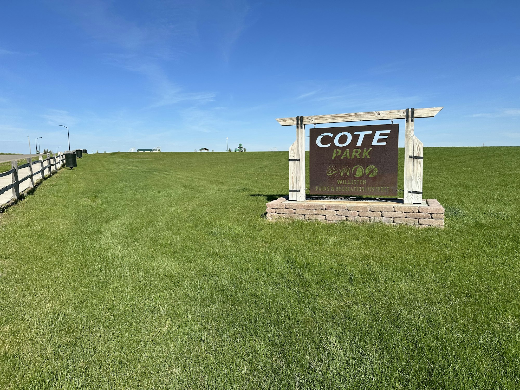 A park sign reading "COTE PARK" with a grass field and blue sky in the background.