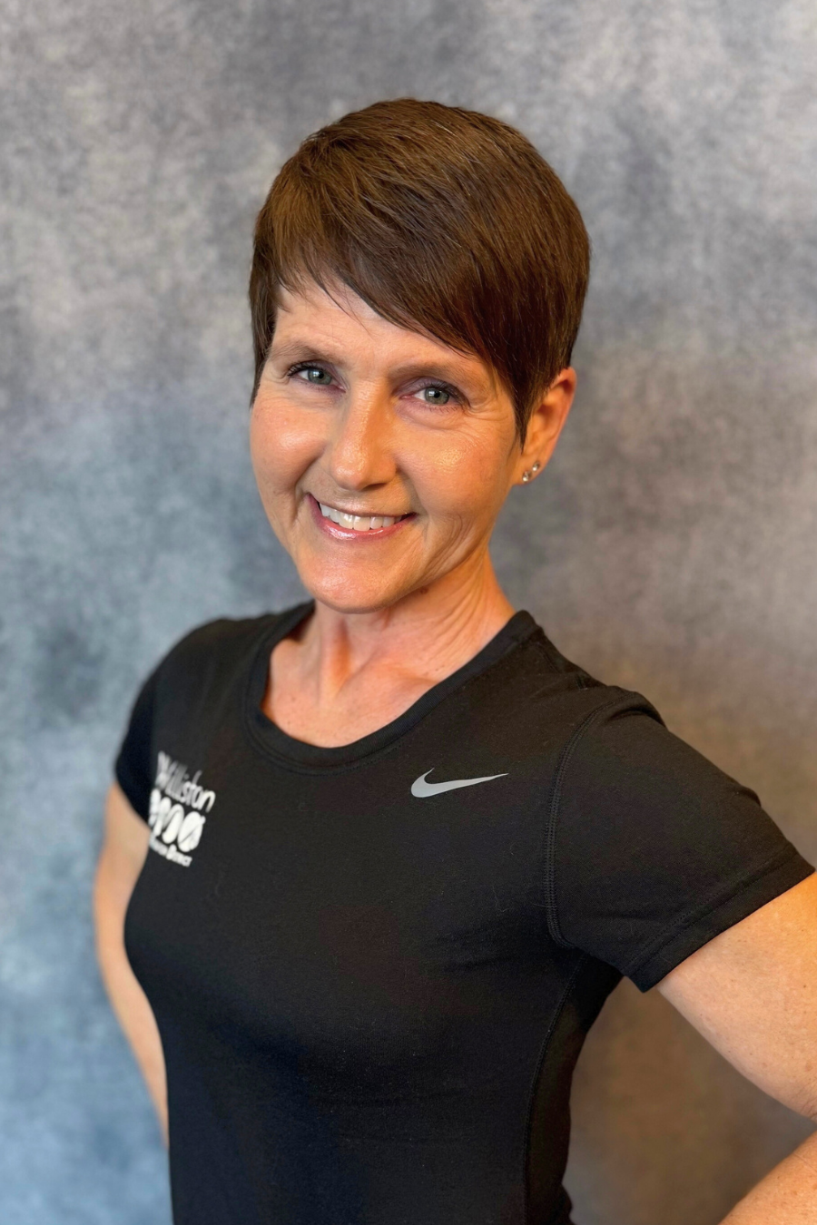 A person with short hair smiles, wearing a black Nike shirt, against a gray background.
