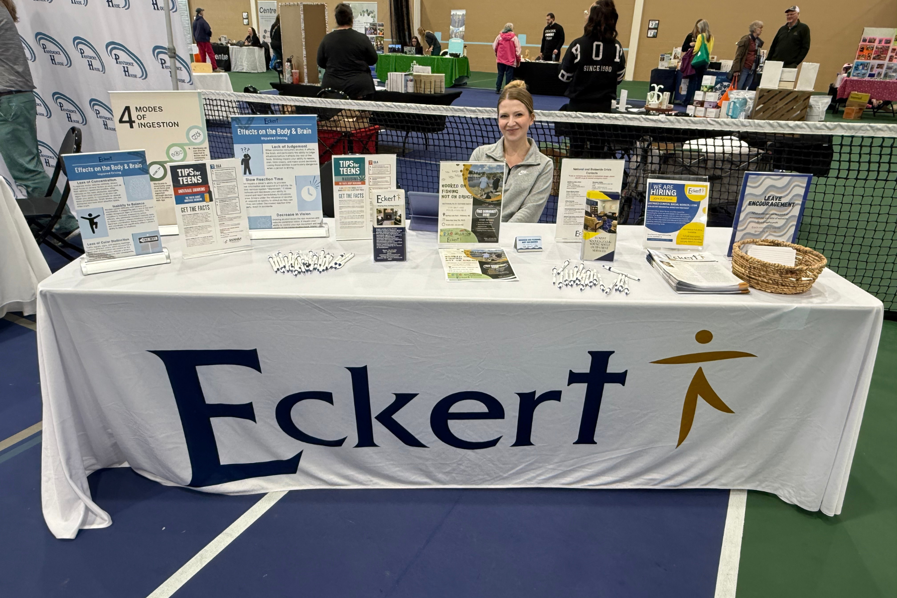 A table with an "Eckert" display, showcasing brochures about effects on the body and brain, with a smiling representative.