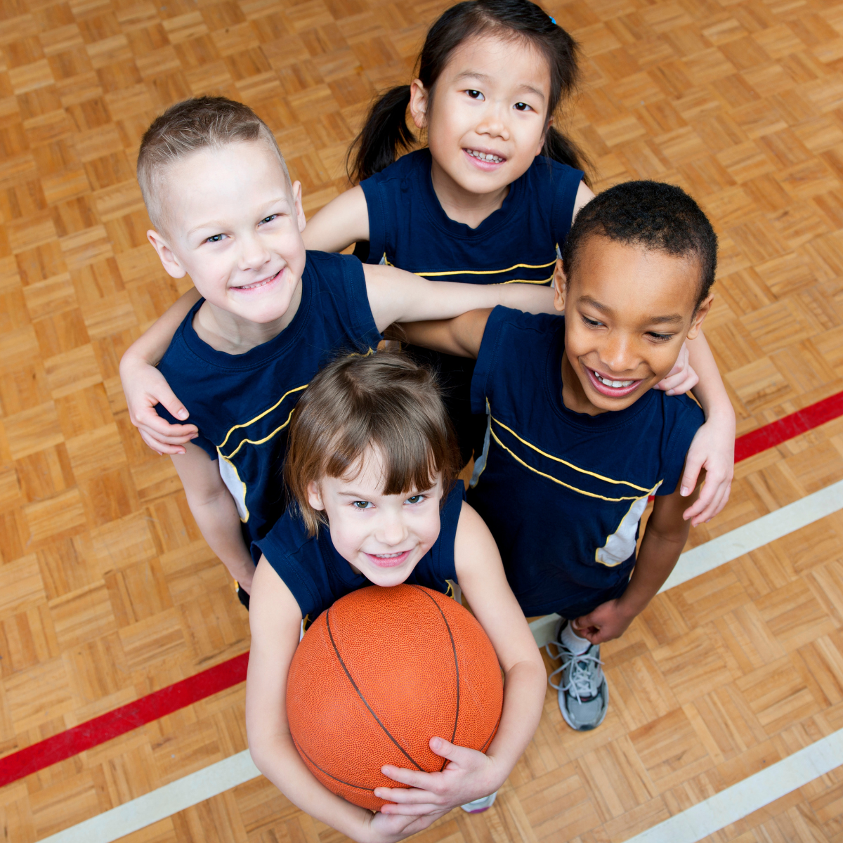 Four children in sports attire smiling with a basketball, shot from above.