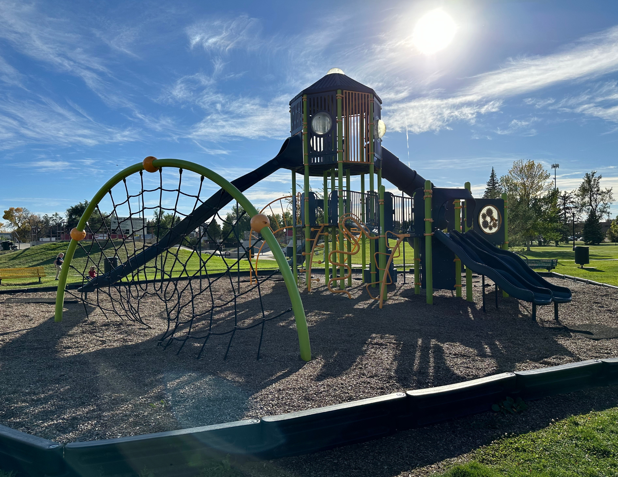 A sunny playground with slides, climbing structures, and a web net.