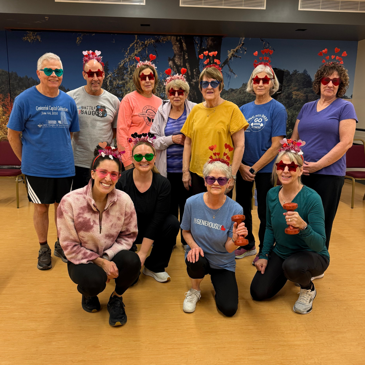 A fun group of people wearing heart-themed glasses and accessories, posing together, likely after a workout or fitness class.