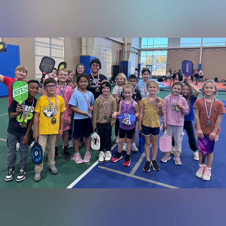 A group of children with medals and paddles, on an indoor court.