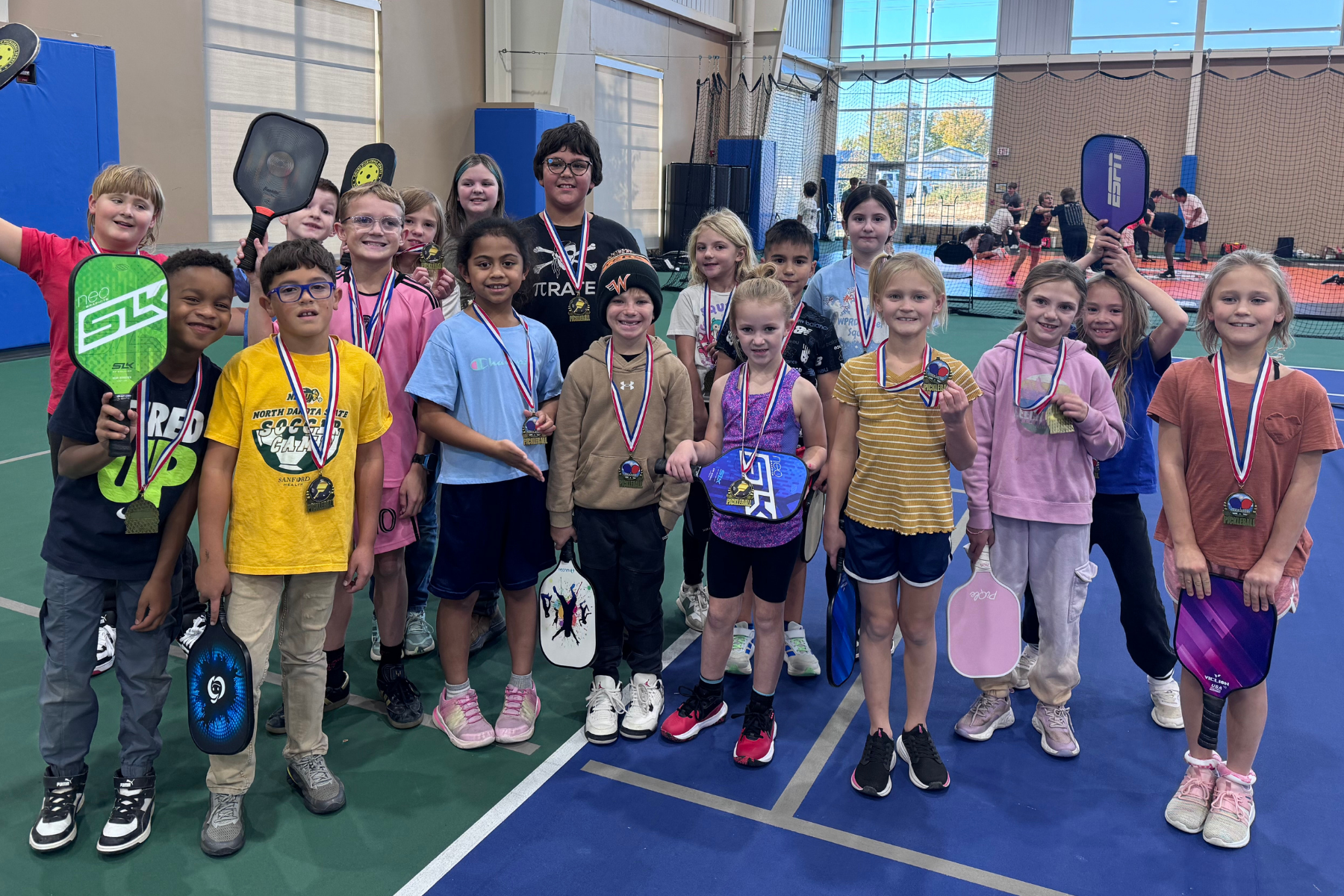 A group of children with medals and paddles, on an indoor court.
