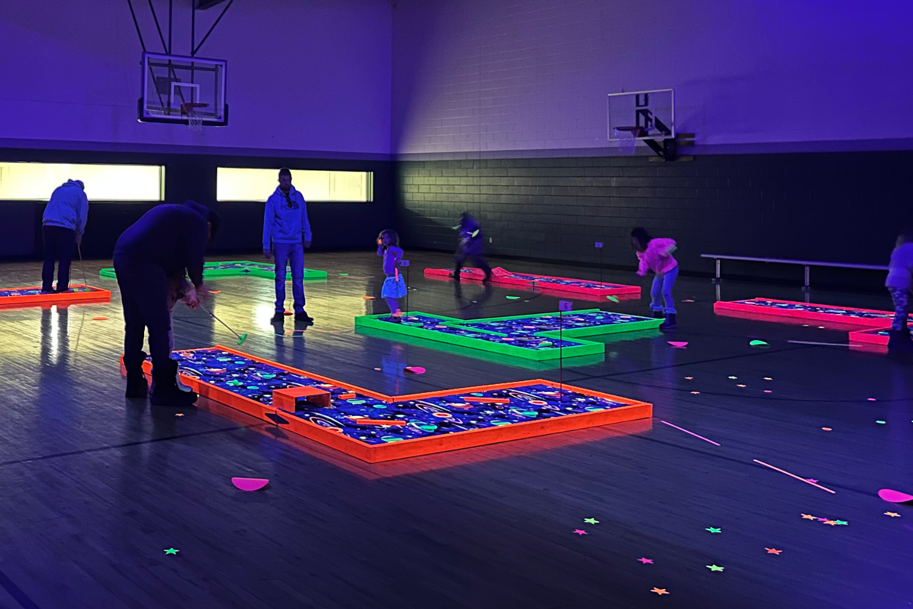 People playing glow-in-the-dark mini-golf in an indoor gymnasium.