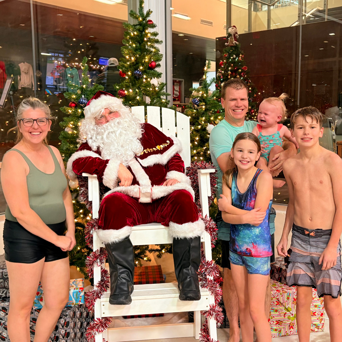 A family poses with Santa Claus in swimwear, surrounded by festive decorations and Christmas gifts.