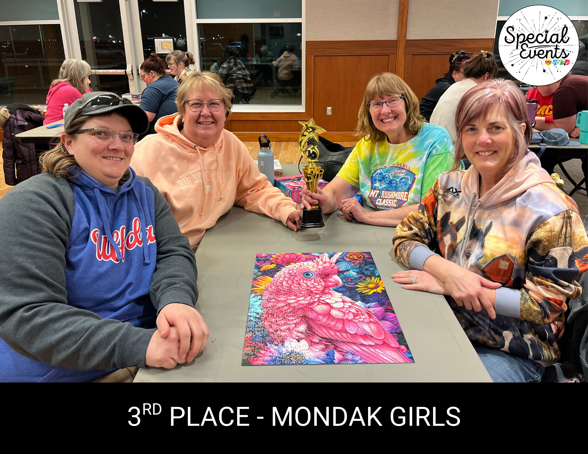 Four women celebrate their 3rd place win, posing with a trophy and a colorful jigsaw puzzle at a special event.