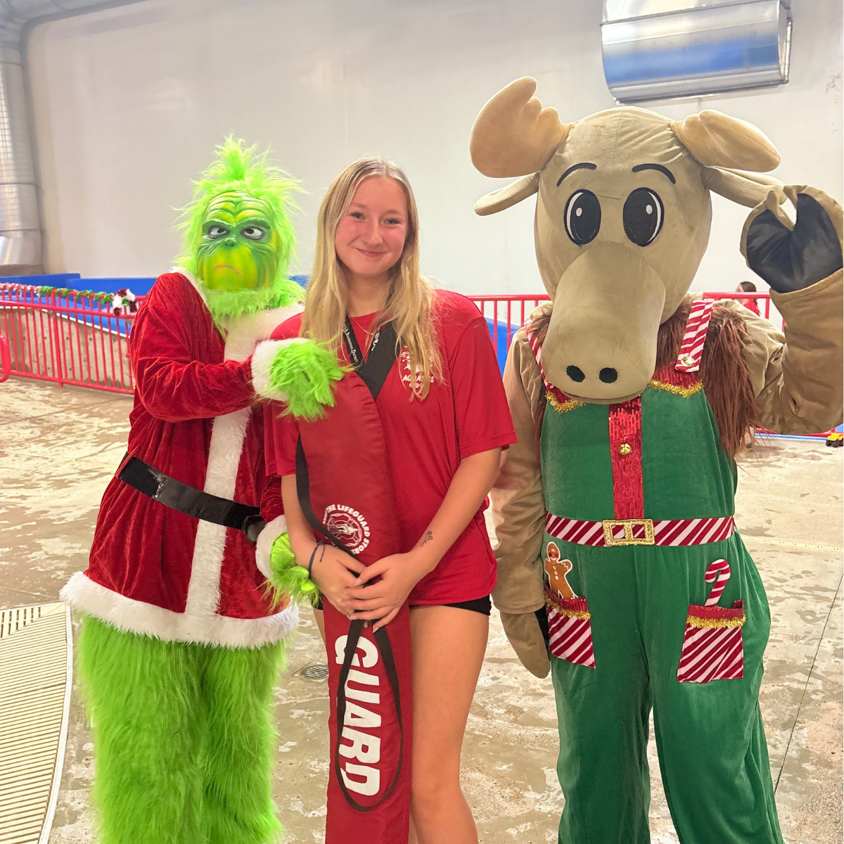 The Grinch and a moose mascot pose with a lifeguard in a festive setting.