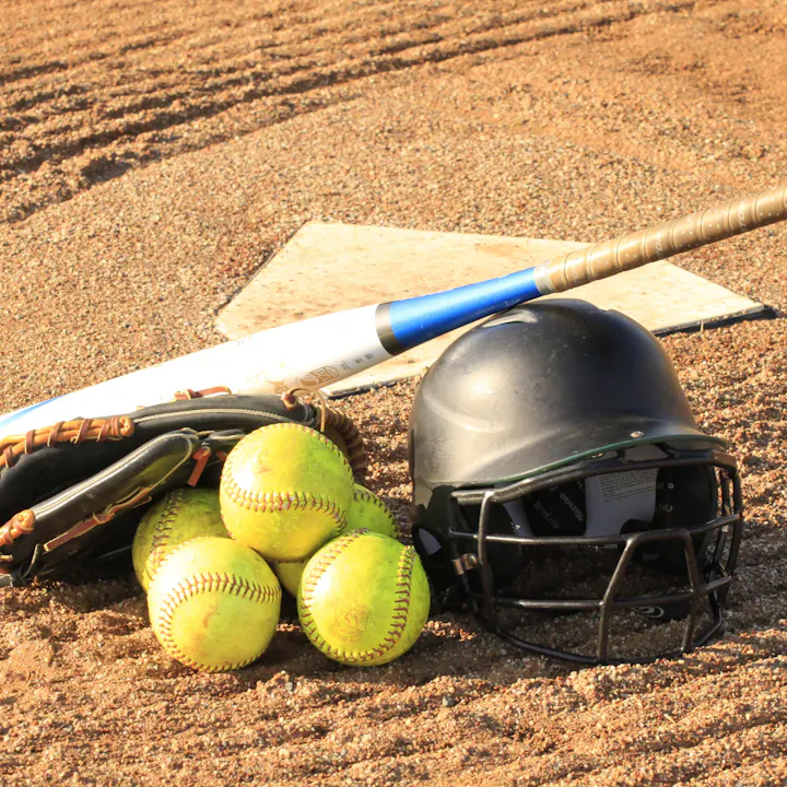 Baseball gear with a bat, helmet, glove, and balls on a dusty field.