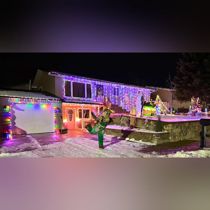 House adorned with colorful Christmas lights, inflatable holiday characters, and a person in a festive costume.