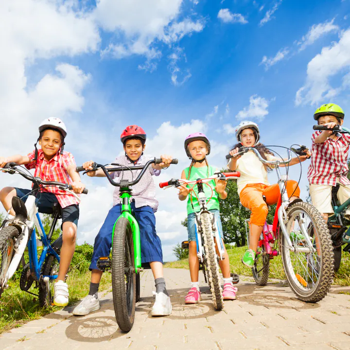 Group of smiling kids on bicycles wearing helmets outdoors.