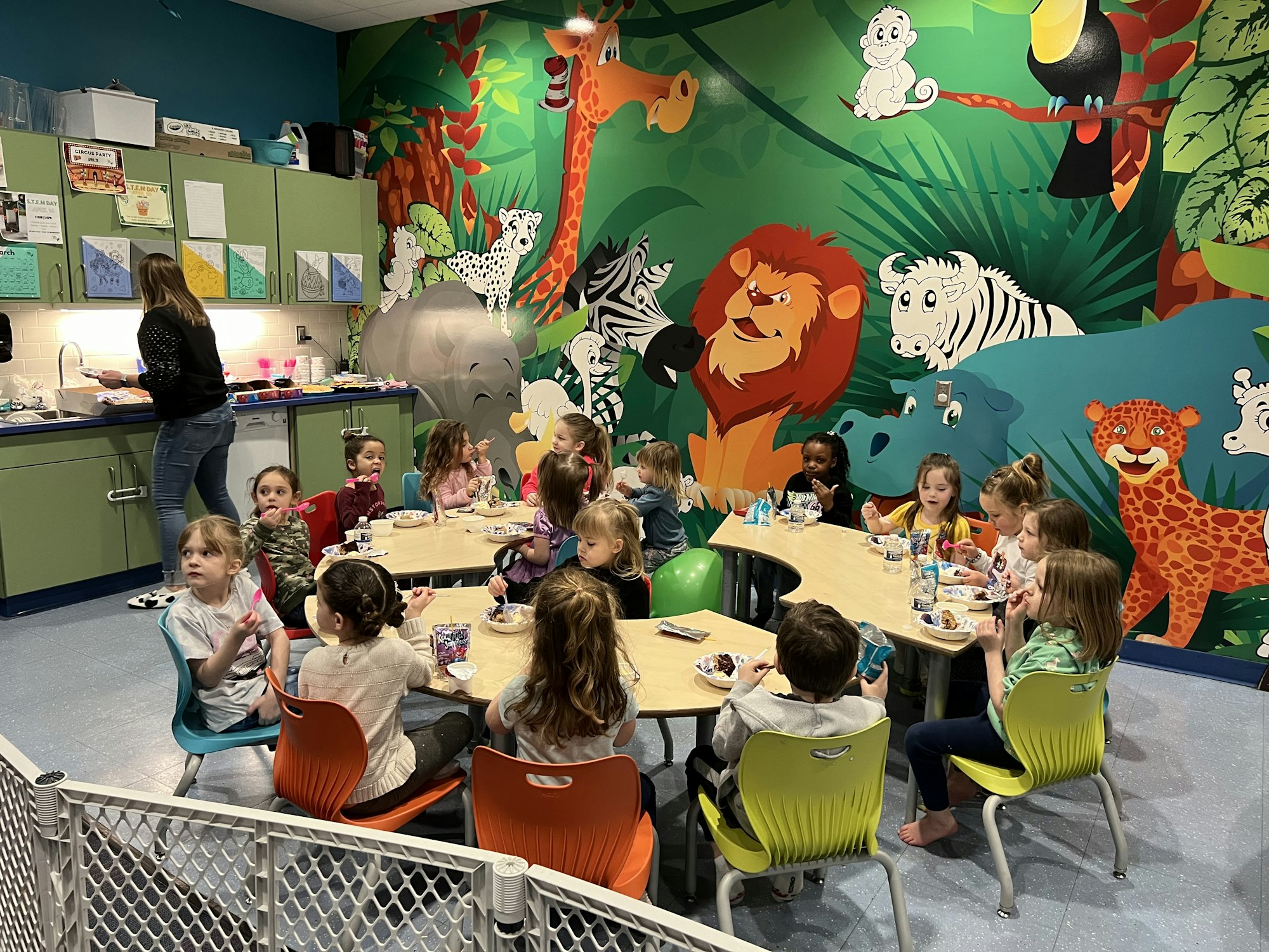 Children eating at tables in a colorful room with jungle animal murals.