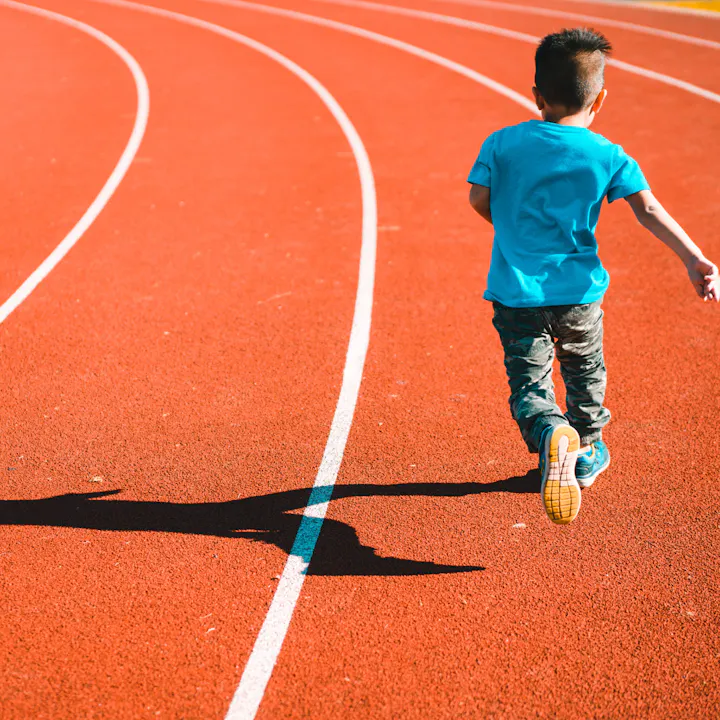 Child running on a red track, casting a shadow.