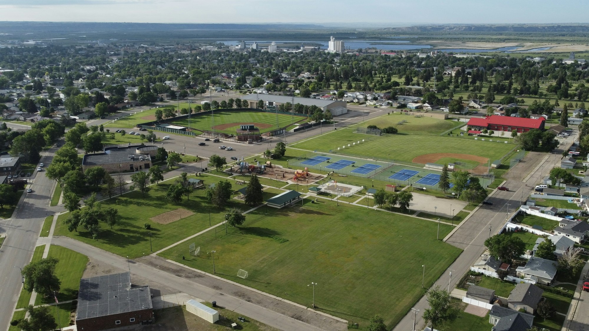 Aerial view of a town with residential areas, a baseball field, tennis courts, and green spaces.