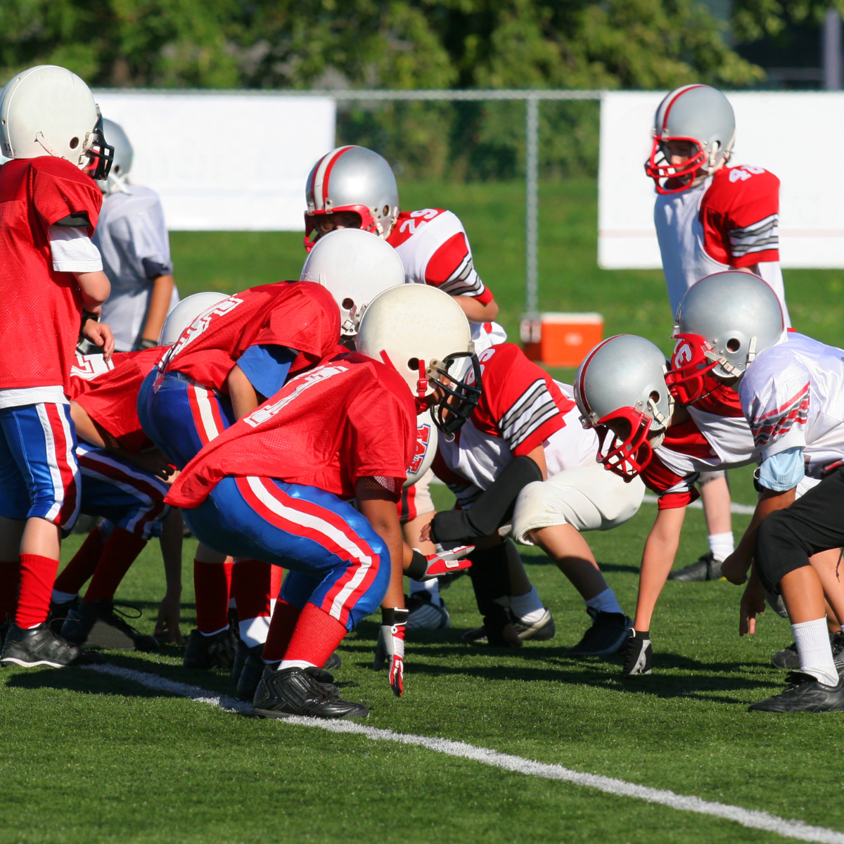 Youth football players in helmets and pads lined up on the field.