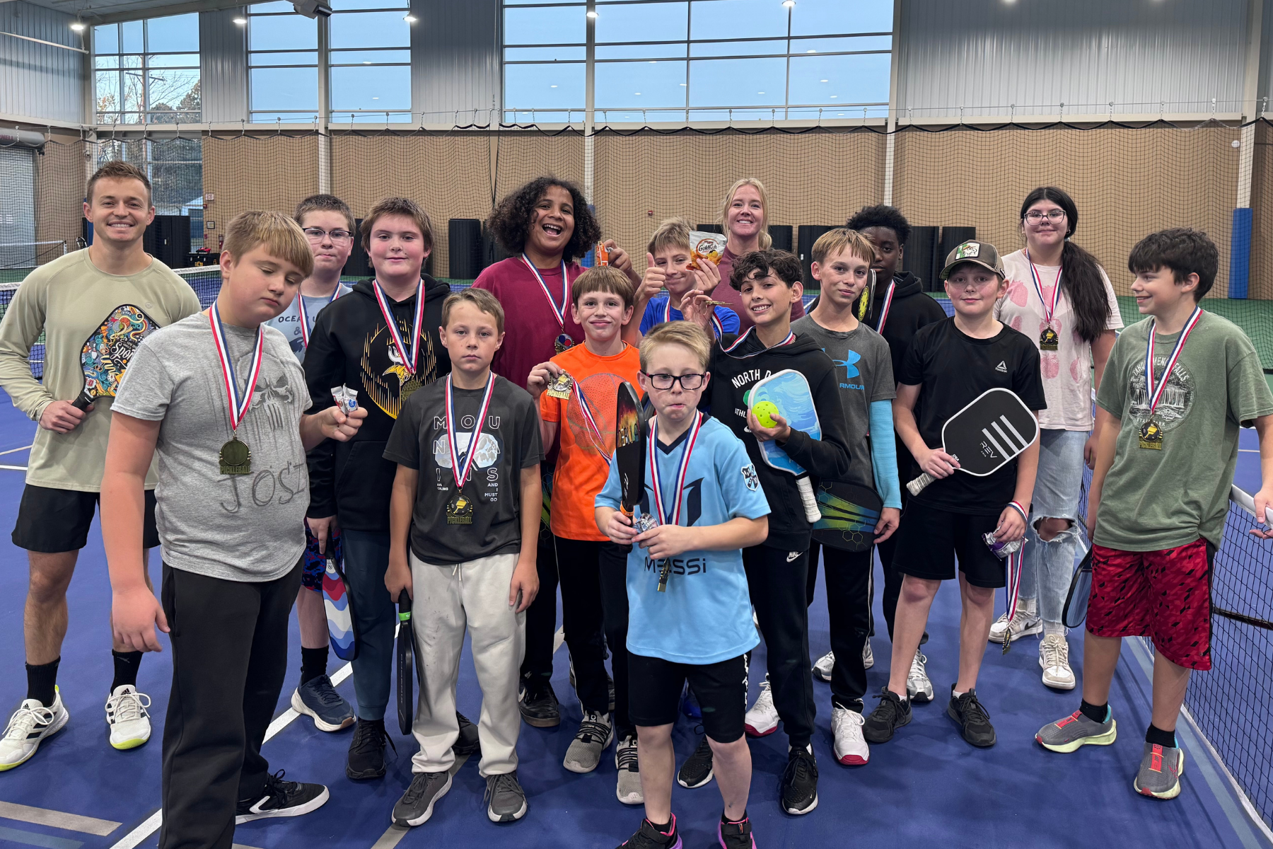 Group of kids and adults with medals and paddles on an indoor court, posing happily for the camera.