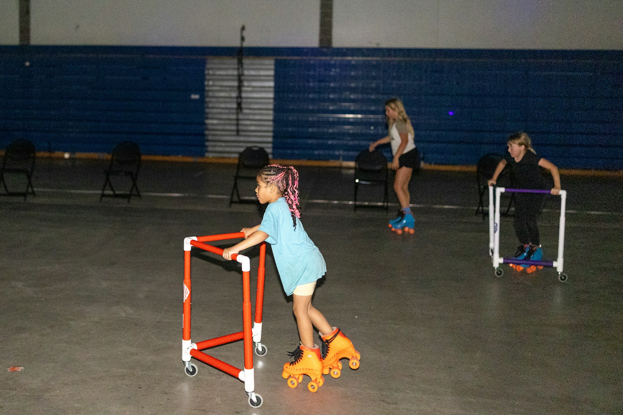 Three people are roller skating indoors using support frames.