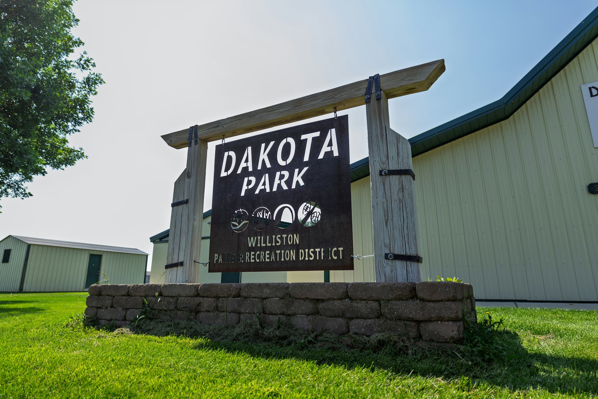 A sign for Dakota Park in Williston, part of the Recreation District, with green grass and buildings in the background.