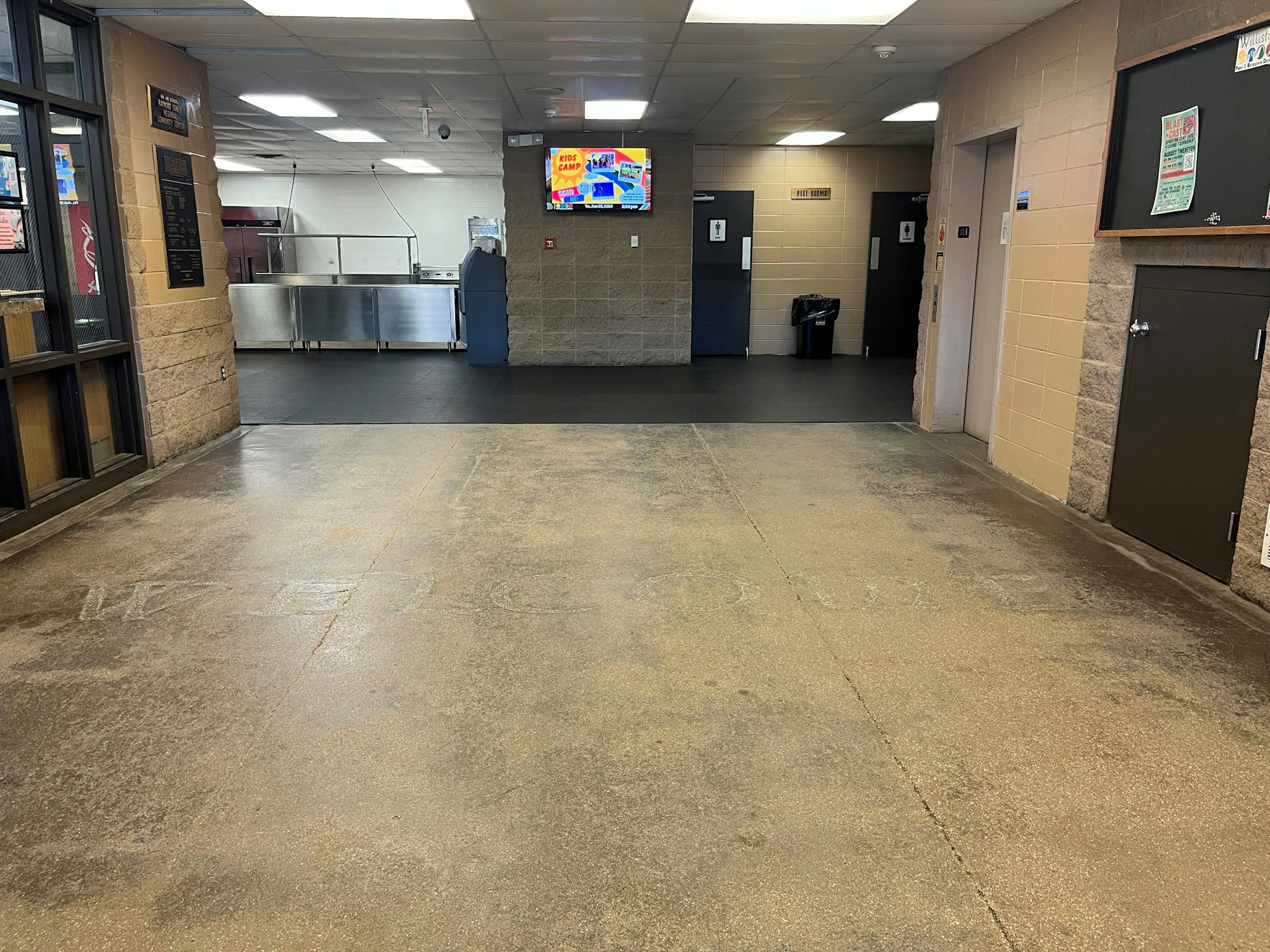 An empty fast-food restaurant interior with menu boards, a service counter, trash bin, and restrooms.