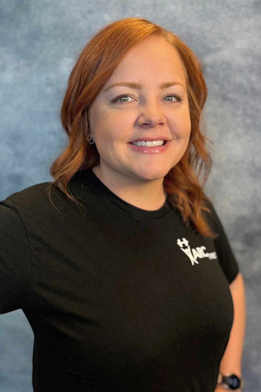 Someone smiling in a black shirt with a blurred backdrop.