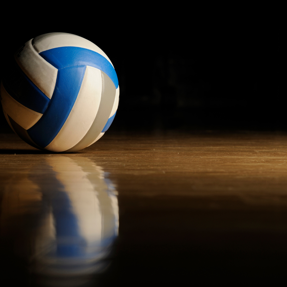 A volleyball on a shiny floor with dramatic lighting and reflection.