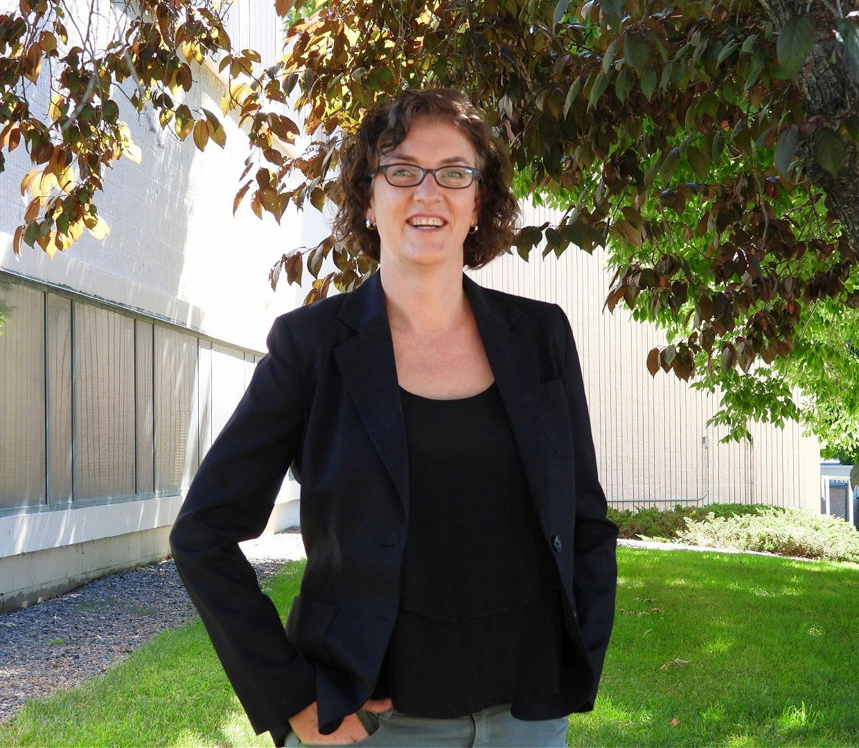 A person smiling outdoors near a tree with green and brown leaves.