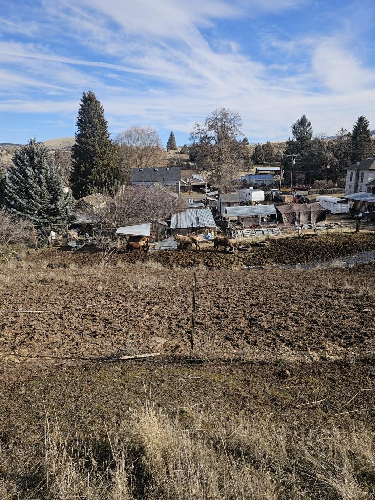 Rural scene with barns, horses, trees, and houses under a blue sky with scattered clouds.