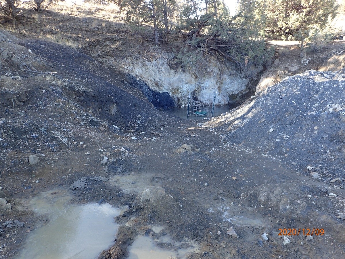A waterlogged excavation site with a pool and a cart, surrounded by earth and rocks.