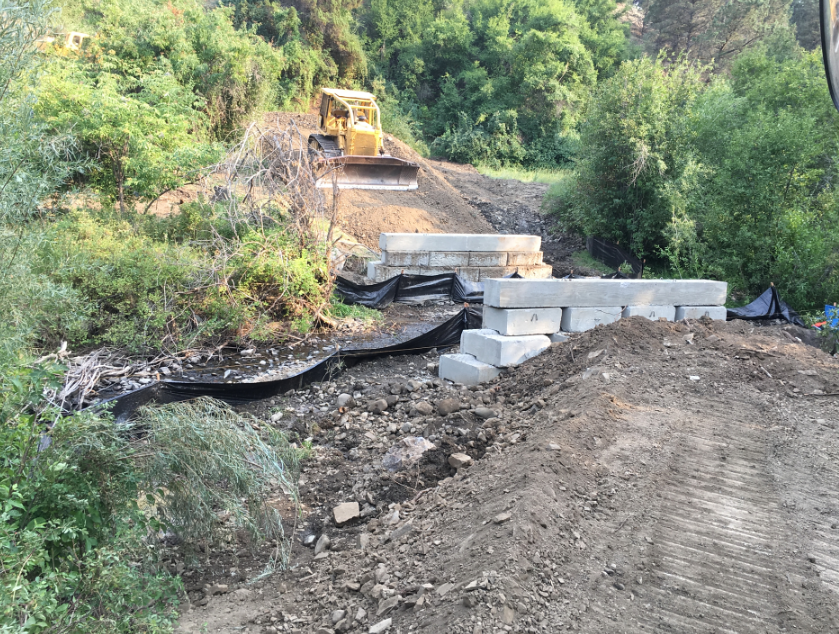 Bulldozer on a dirt mound, concrete blocks, construction site, greenery around.