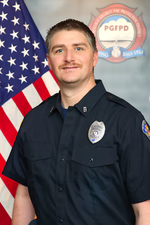 The image features a man in a dark uniform with fire department badges, posed in front of an American flag and department emblem.