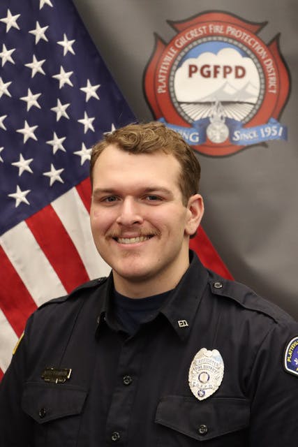 The image features a uniformed firefighter posing in front of an American flag and a logo for the fire protection district.