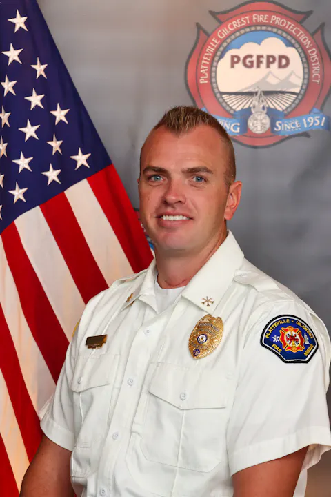 The image features a firefighter in a uniform, smiling, with an American flag and a fire department logo in the background.