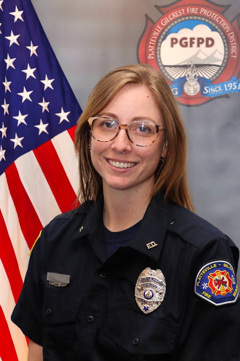 A person in a firefighter uniform with badges stands in front of an American flag and PGFPD emblem.