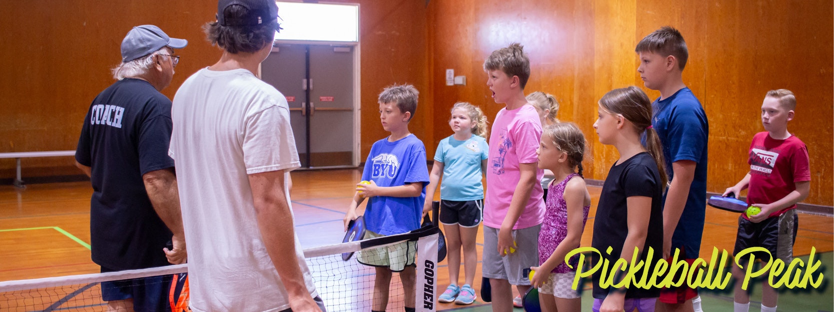 A coach instructs kids on pickleball in a gym, labeled "Pickleball Peak."