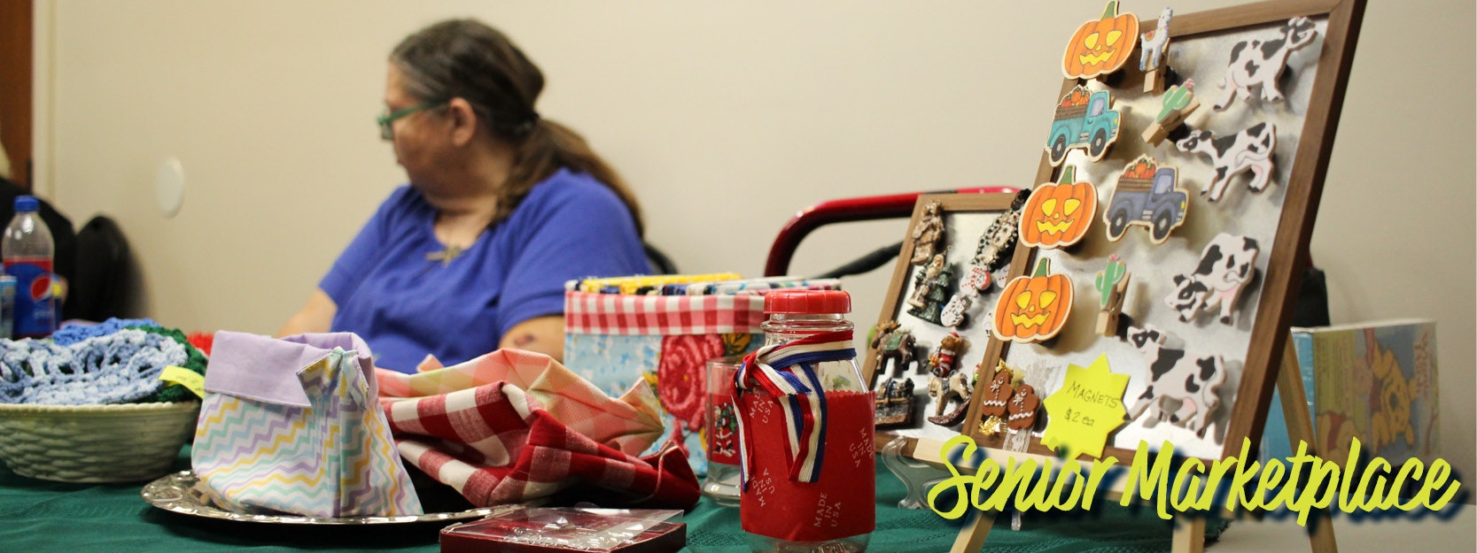 Senior marketplace with crafts and magnets for sale on a table, attended by a person.