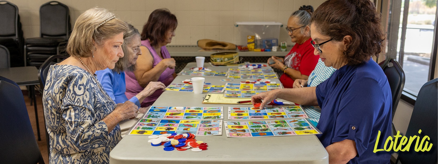 A group of people play Lotería, using cards and markers at a table.