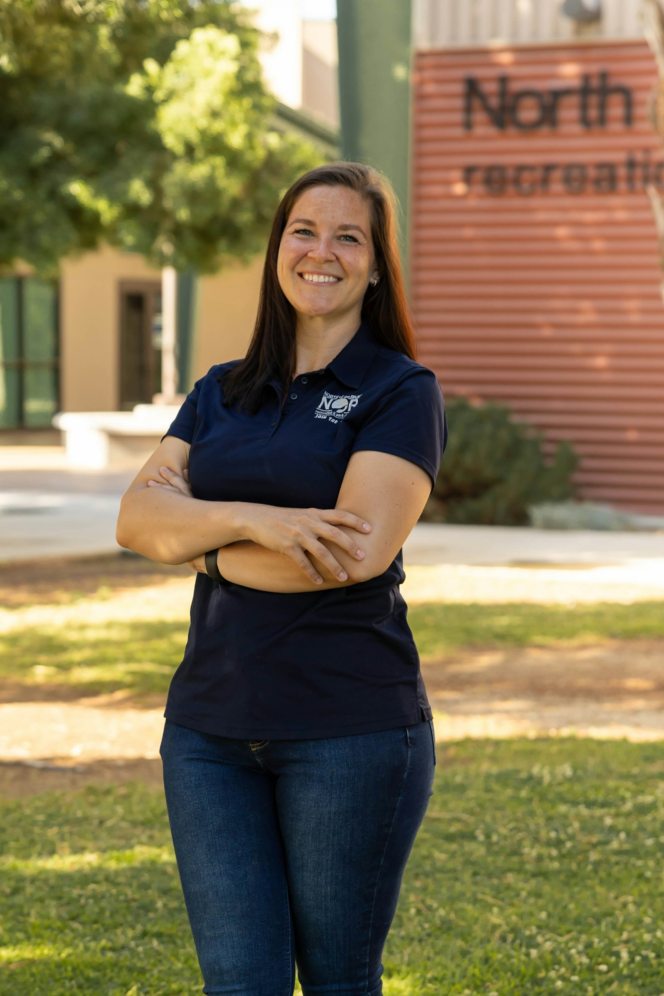 A woman smiling with arms crossed, standing outdoors near a building with a "North recreation" sign.