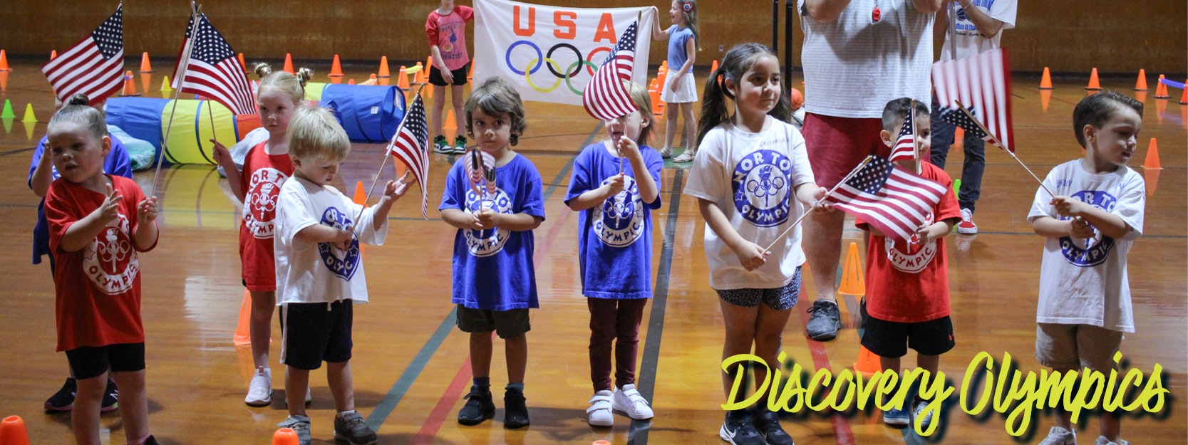 Children holding American flags at an indoor "Discovery Olympics" event.